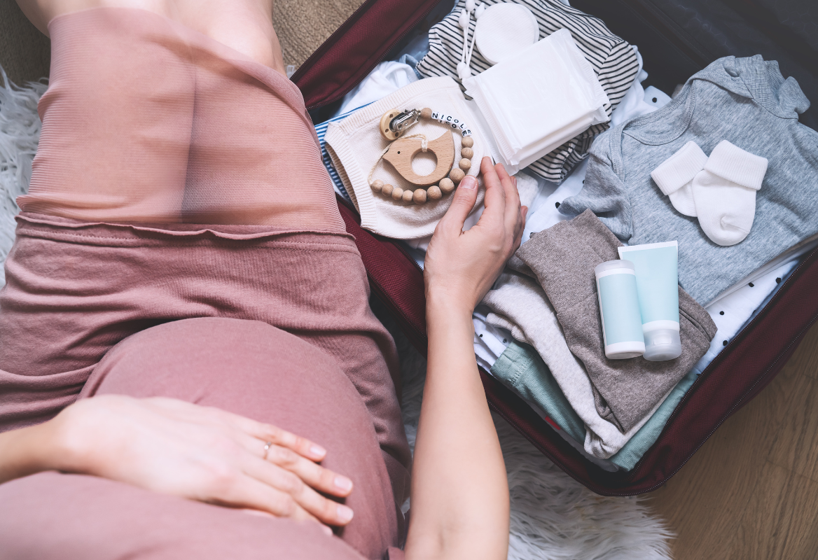 pregnant lady with hand on stomach, sitting next to a packed hospital bag 